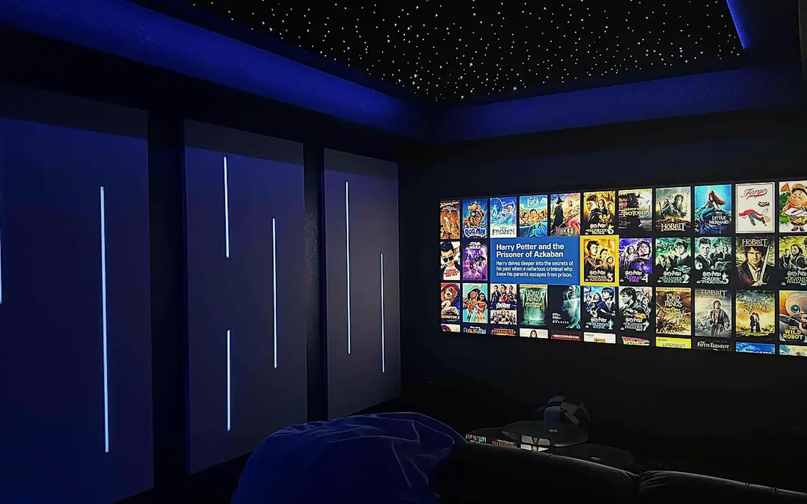 Dark home theater with LED-lit wall panels, a blue star ceiling and a grid of movie posters on the screen