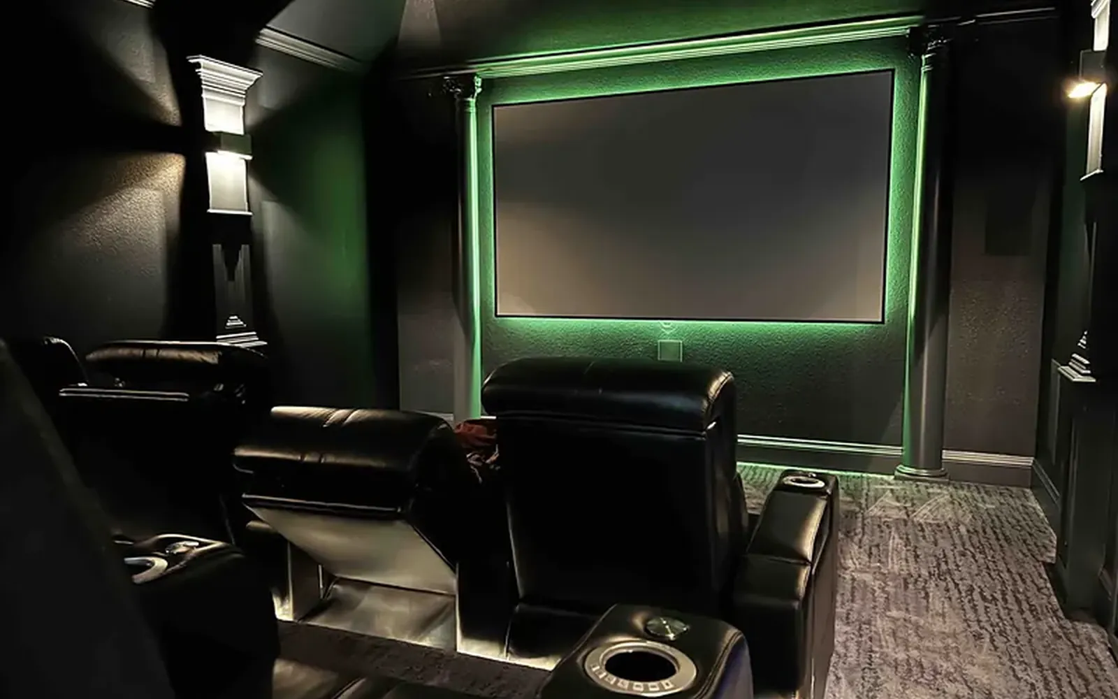 Home theater with a green accent light behind the screen wall and leather recliners