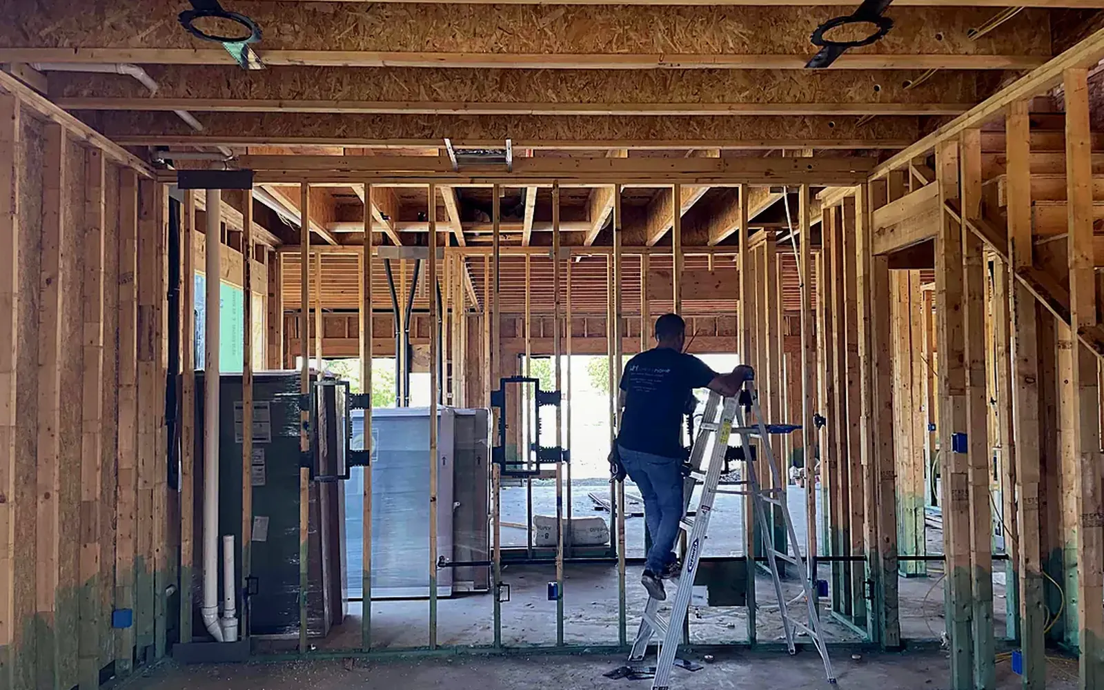 Interior of a framed house during low-voltage rough-in with a technician working from a ladder