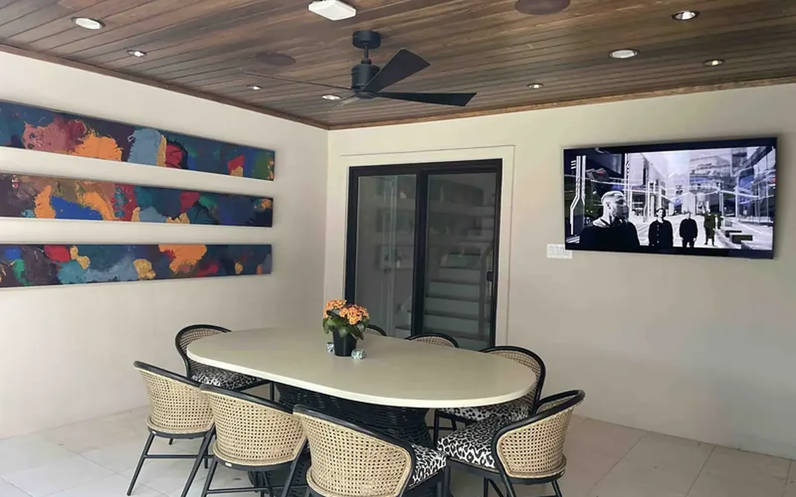 Covered patio dining area on a WH Technologies project with a wall-mounted outdoor TV facing a long table under a finished ceiling