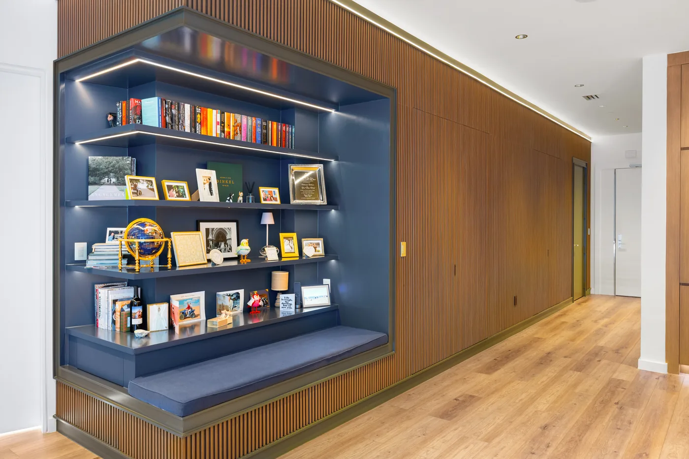 Built-in display niche in deep blue with lit shelves set into walnut millwork
