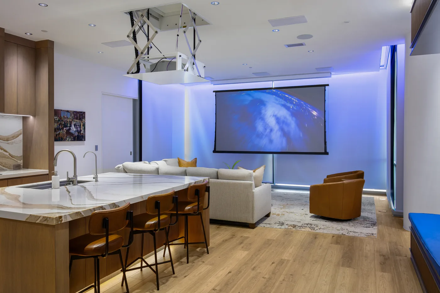The living room at night with the projection screen down and a blue cove light above it