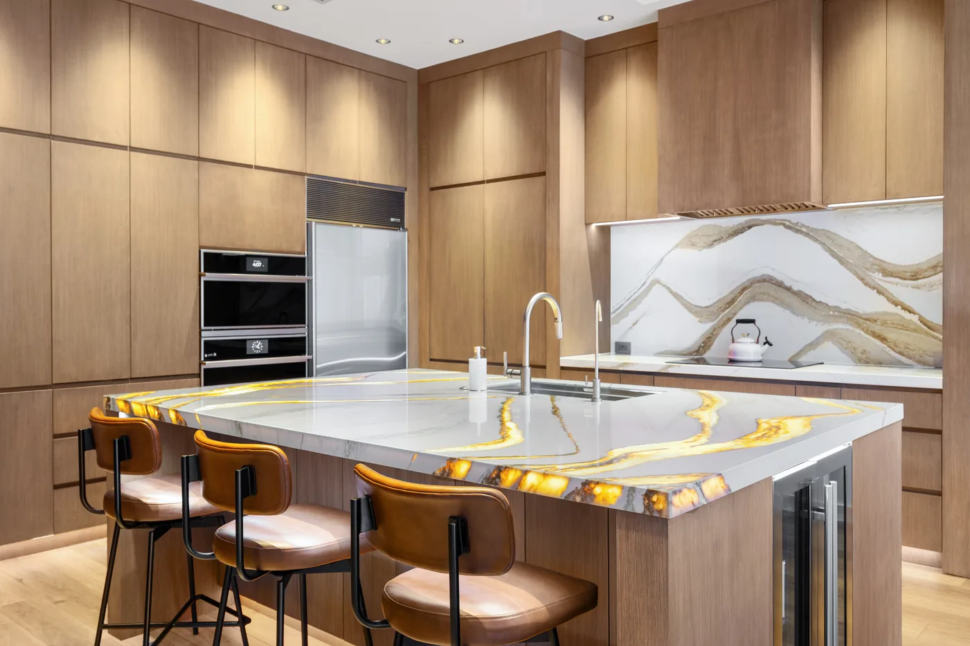 Kitchen island with a lit onyx top by day, brass faucet and walnut cabinets