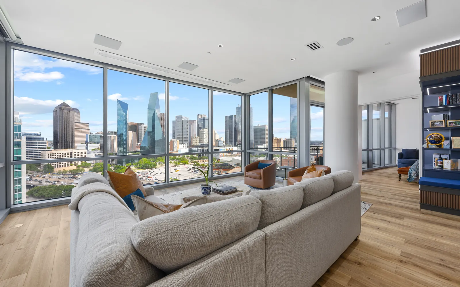 Living room of a Dallas high-rise condo with floor-to-ceiling glass, a sectional sofa and the downtown skyline behind