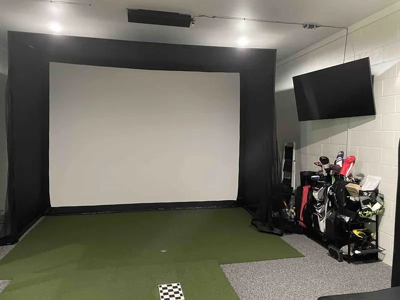 Golf simulator room with a projection screen and hitting mat