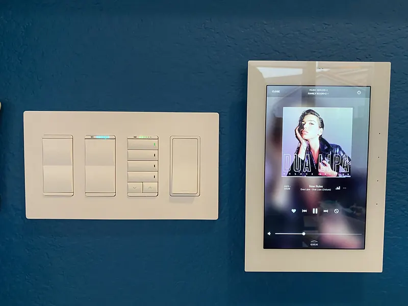 Lighting keypad and a wall-mounted touch panel showing music on a blue wall