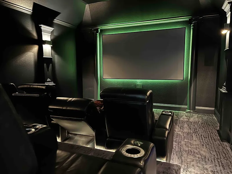 Home theater with leather recliners and green accent lighting around the screen
