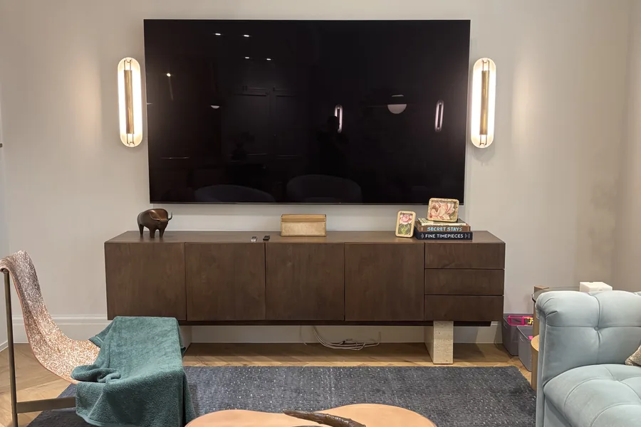 Living room with a wall-mounted TV between two lit sconces, a console and a tree