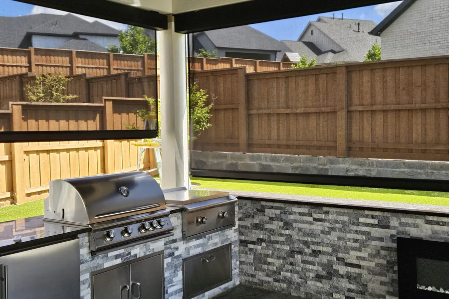 Covered patio with an outdoor kitchen, a stone counter and a wood fence behind