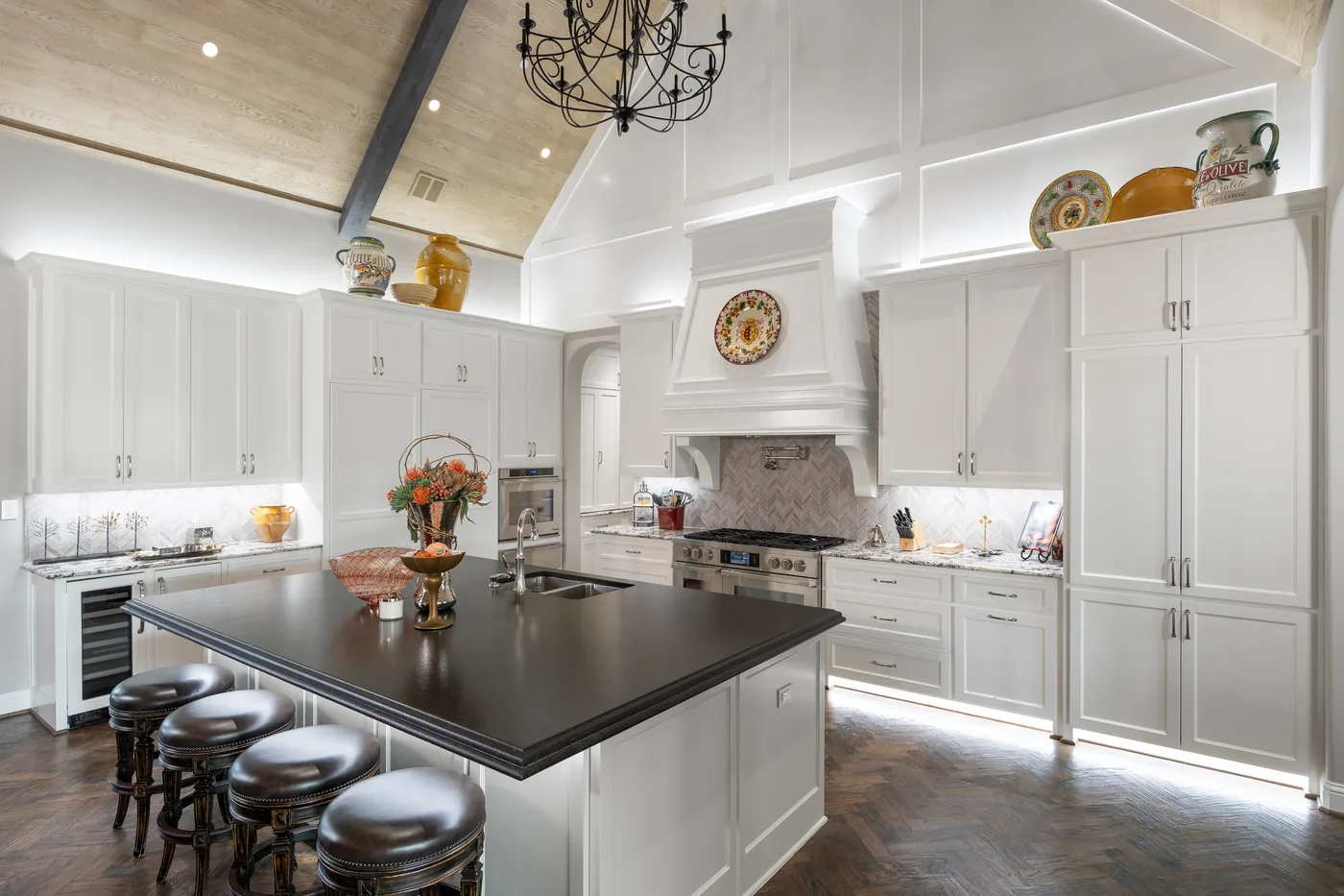 White kitchen with a dark island, under-cabinet light, lit range hood and a vaulted ceiling