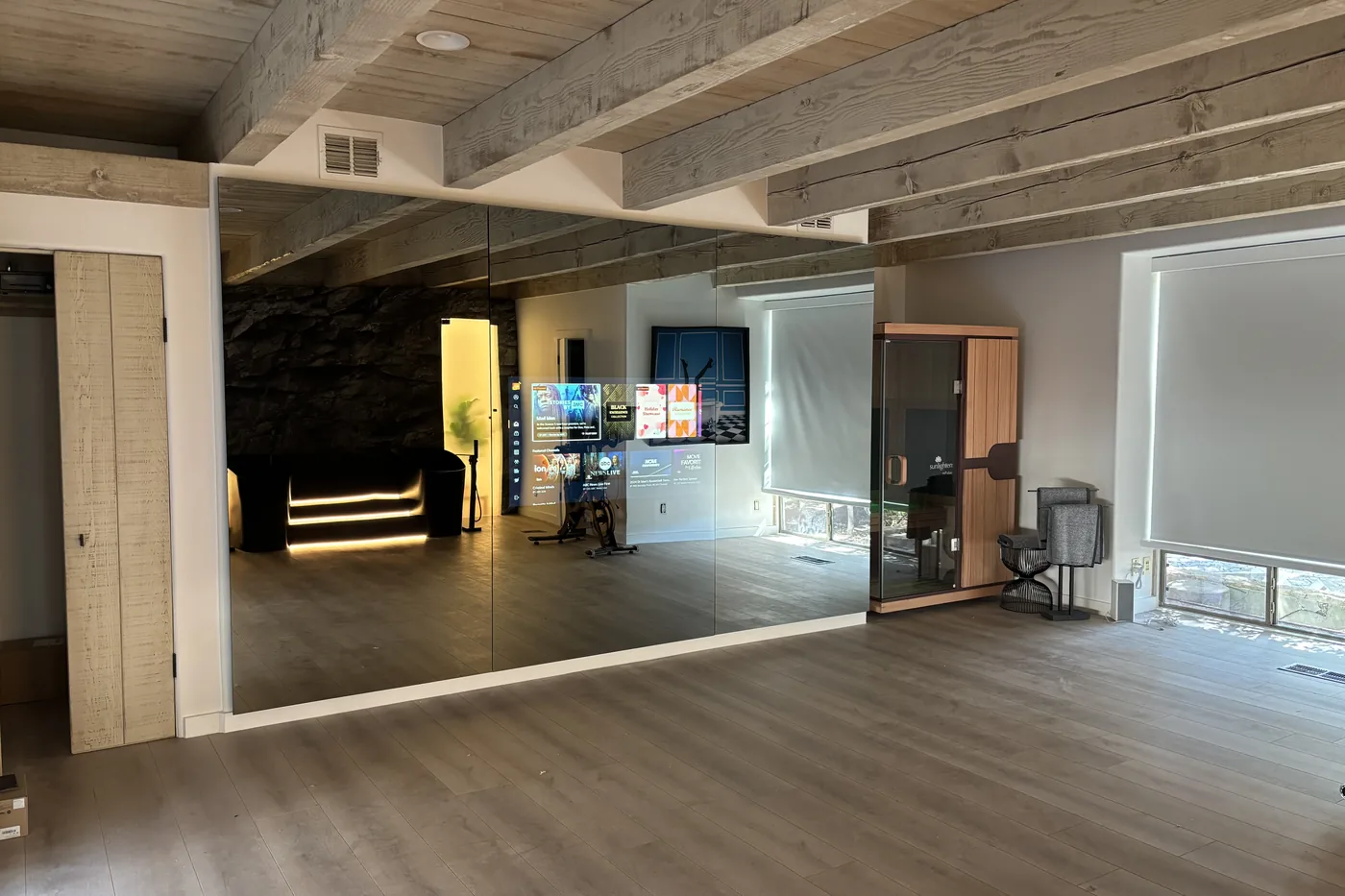 Wide view of the gym with a mirror wall, a stone accent wall, lit panels and exercise equipment