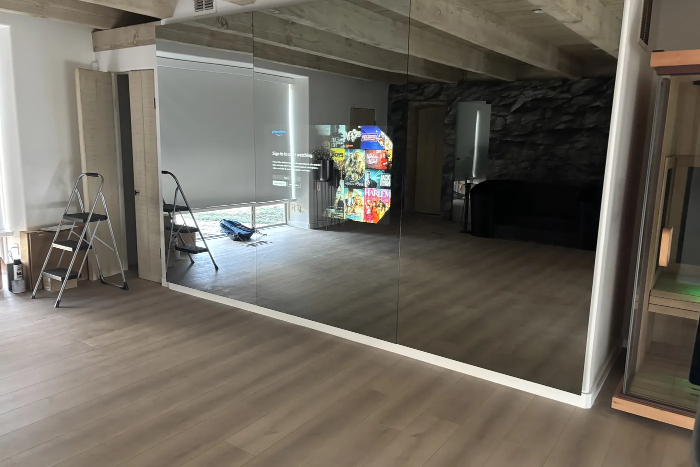 Gym mirror showing a streaming app menu, with a bike and weights in front of it