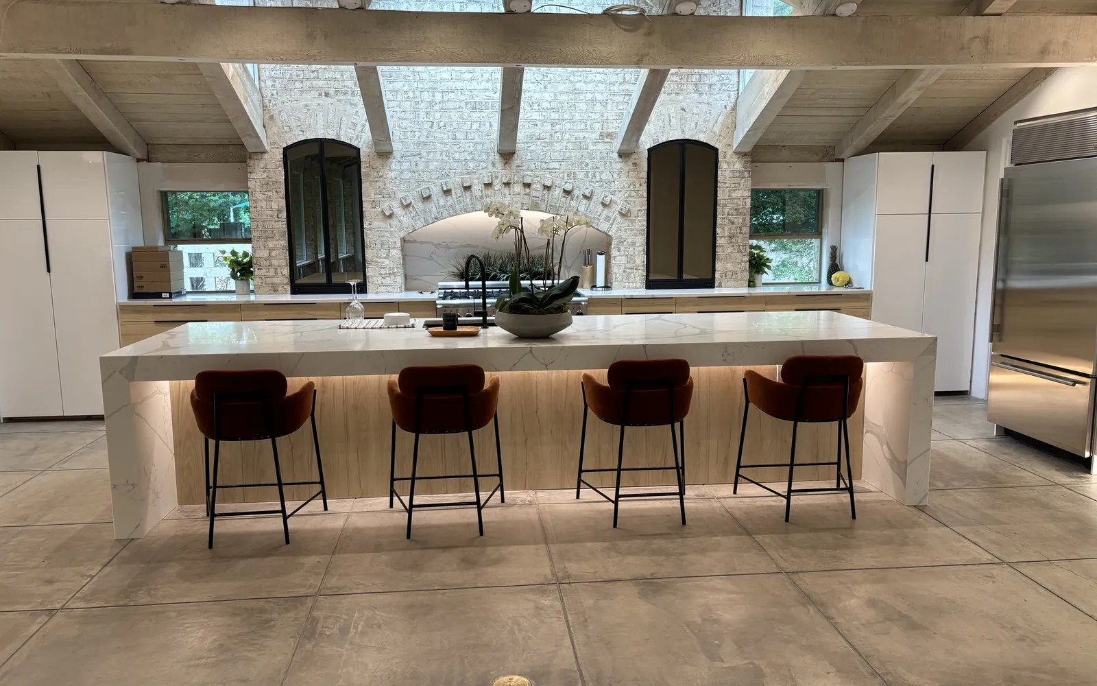 Mid-century kitchen with a vaulted wood ceiling, a stone fireplace wall, a long island with bar stools and warm recessed lighting