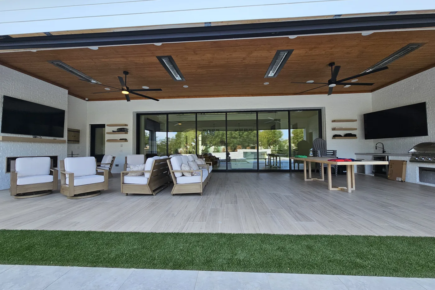 Covered patio with a wood ceiling, two outdoor TVs, fans and lounge seating opening to the pool
