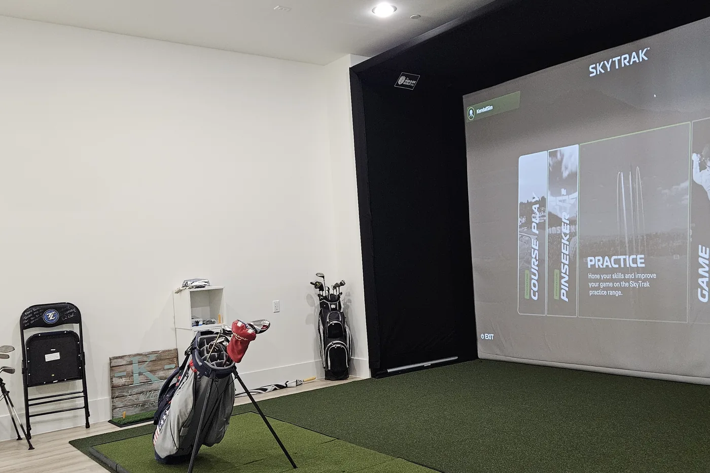Golf simulator bay with a projected course, turf and a golf bag ready to play