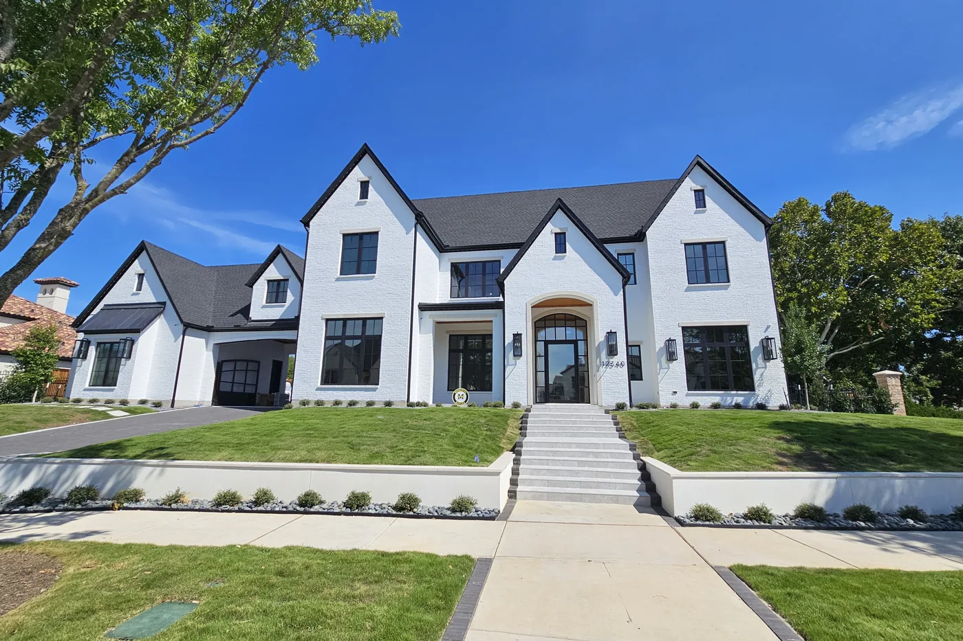 White modern farmhouse with black windows, a live oak and a lawn under a blue sky