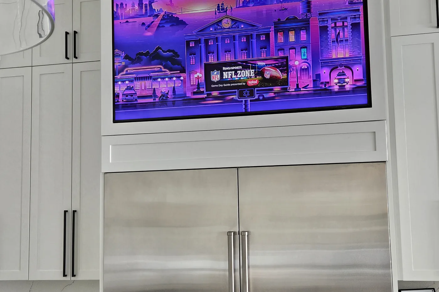 Kitchen with a television built into the cabinetry above the refrigerator