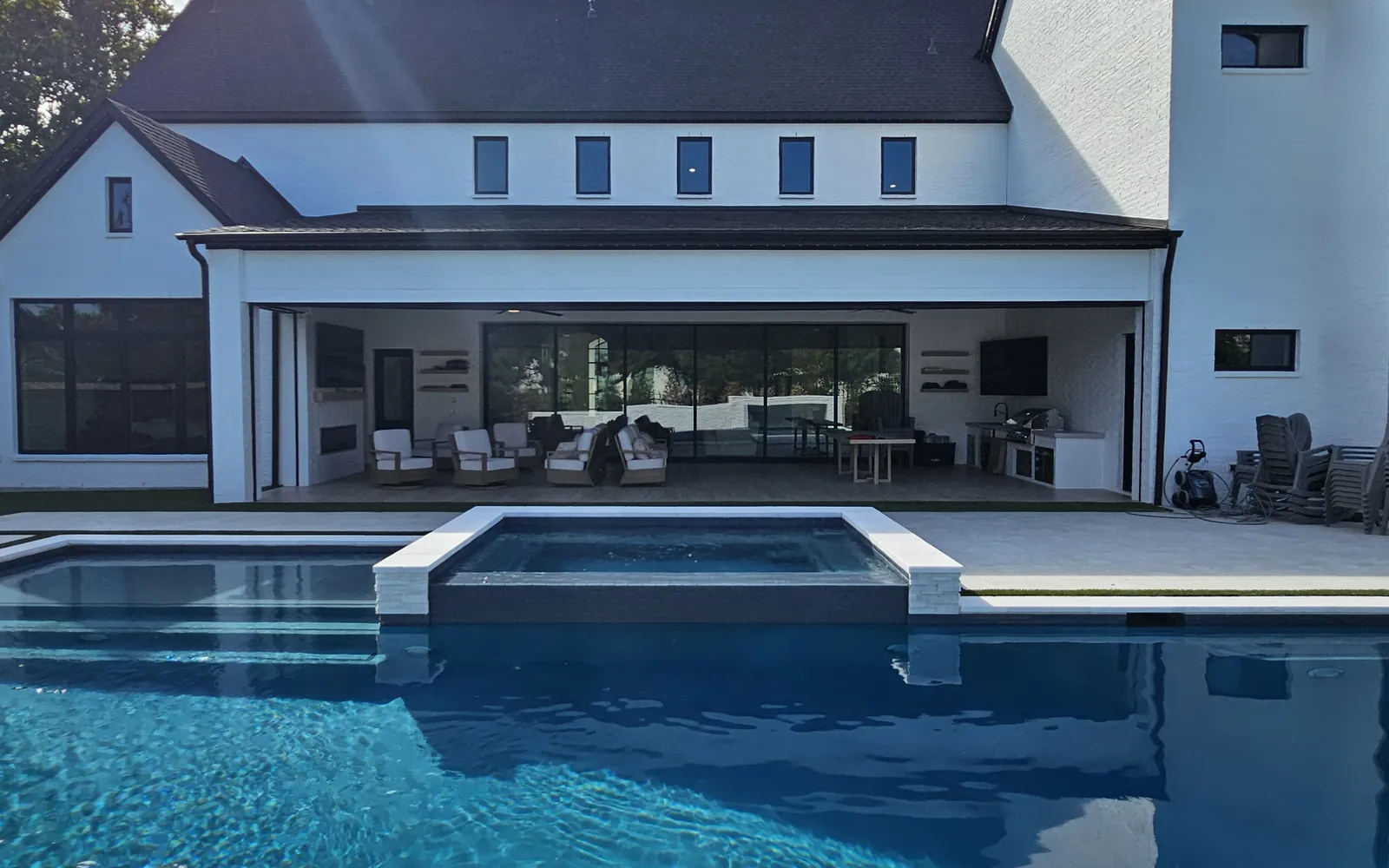 White modern farmhouse in Frisco seen across the pool, with the covered patio open to the backyard