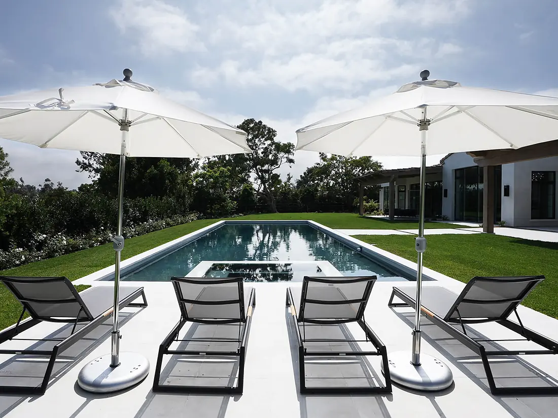 Lap pool with sun loungers and white umbrellas, Sonance outdoor speakers in the landscaping