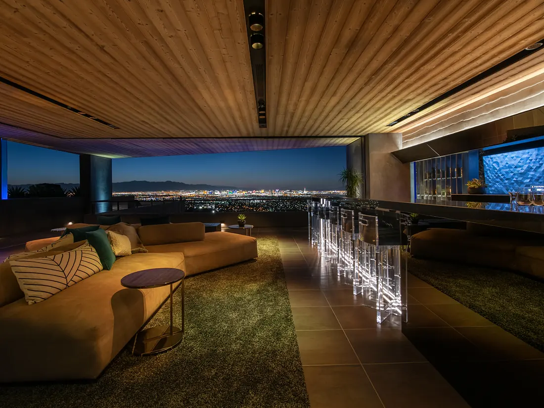 Open-air lounge at dusk with a wood ceiling, a lit bar and a city view, controlled by a Savant system
