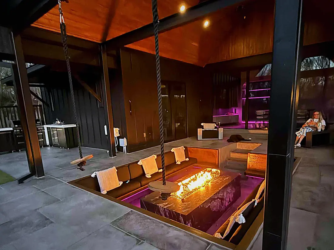 Covered patio at night with a fire pit, outdoor television and lighting under the roof